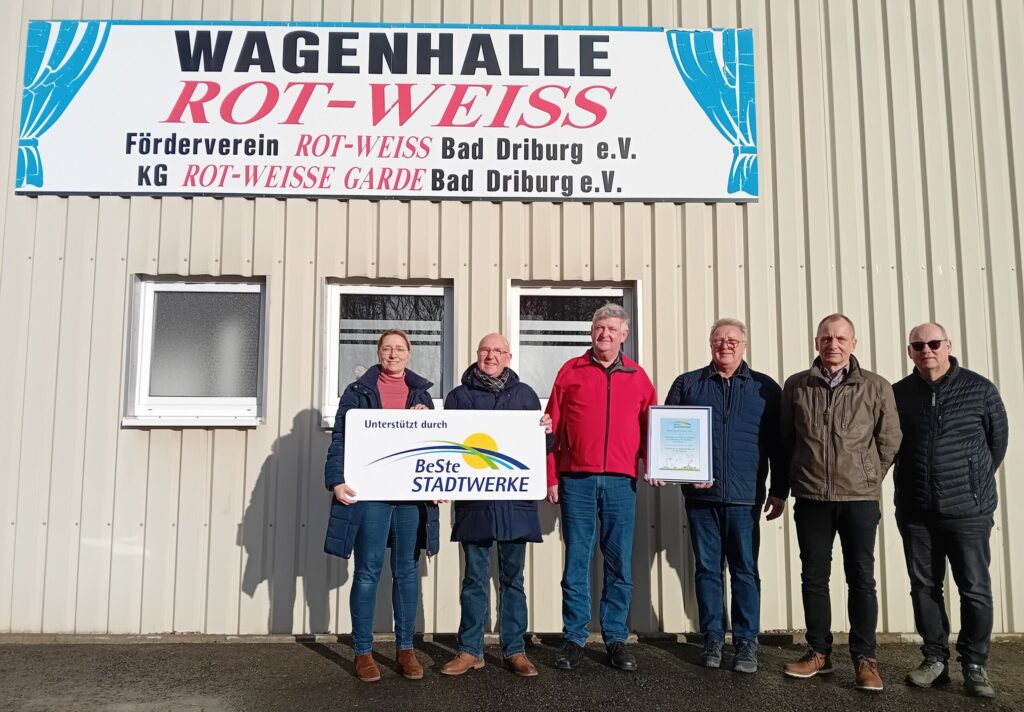 Fünf Personen stehen vor einem Gebäude und halten eine Auszeichnung