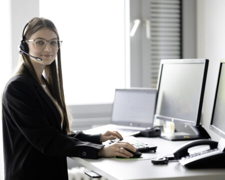 Eine Frau sitzt an einem Schreibtisch mit Monitoren, Telefon und Laptop