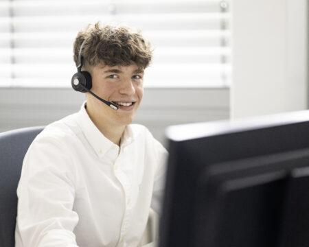 Ein Mann mit Headset sitzt an einem Schreibtisch hinter einem Bildschirm