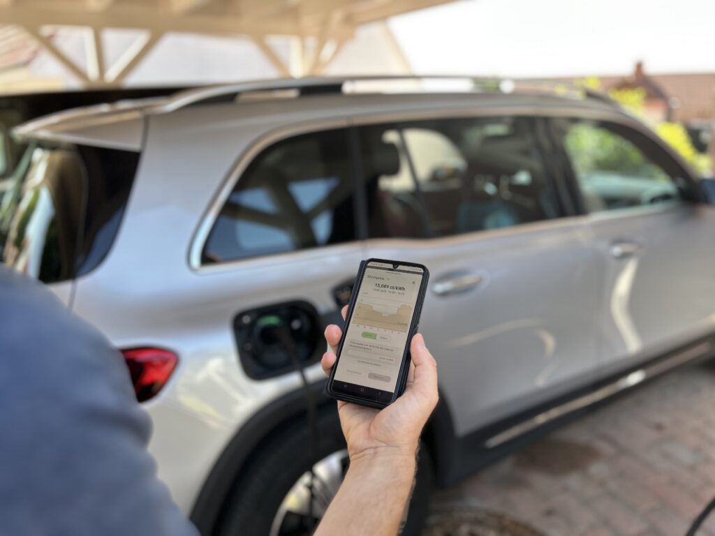 Eine Hand hält ein Handy und beobachtet den Ladevorgang des E-Autos
