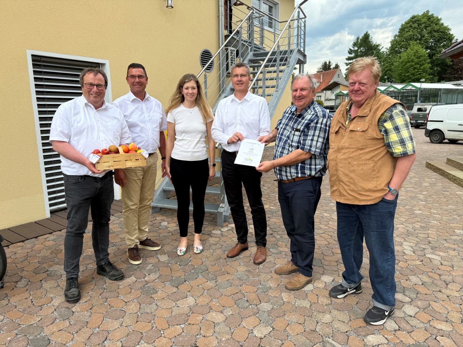 Sechs Personen stehen in einem Halbkreis vor einem Gebäude und halten einen Vertrag in den Händen.