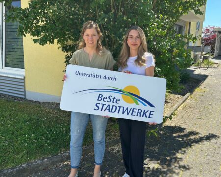 Zwei Frauen stehen mit einem weißen Schild in den Händen vor einem Busch