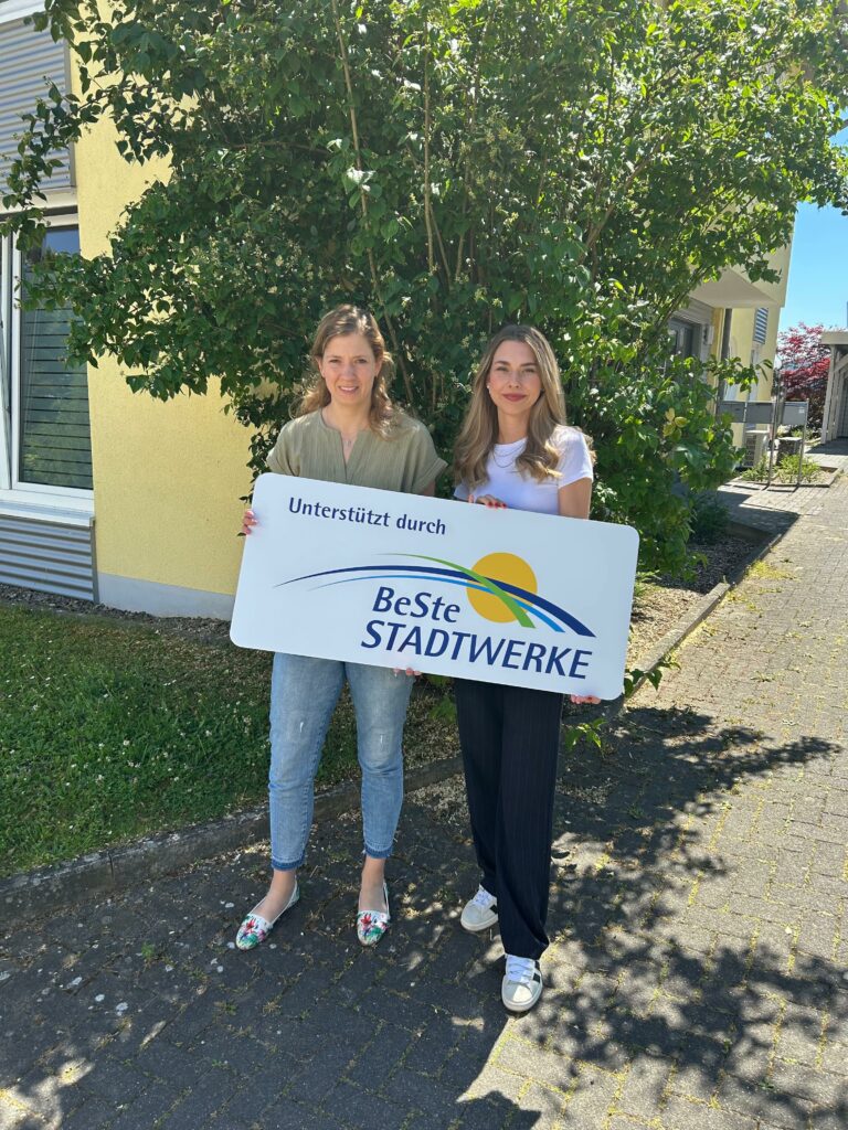Zwei Frauen stehen mit einem weißen Schild in den Händen vor einem Busch