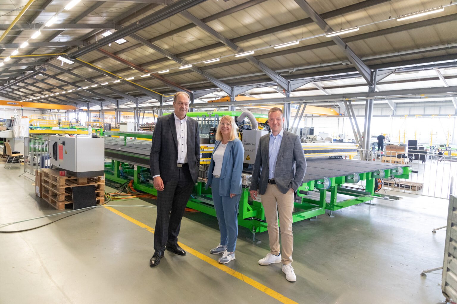 Drei Personen stehen vor einer Industrieanlage in einer Produktionshalle