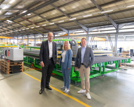 Drei Personen stehen vor einer Industrieanlage in einer Produktionshalle