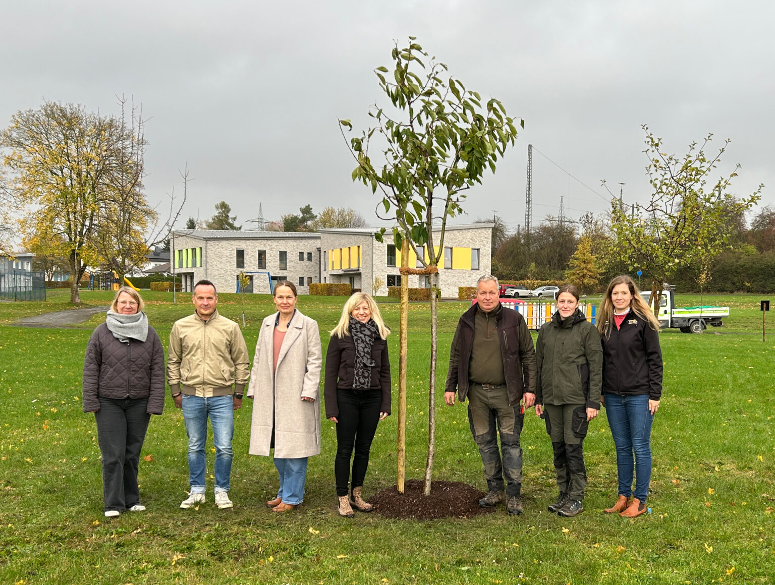 Sieben Personen stehen neben einem neu eingepflanzten Obstbaum