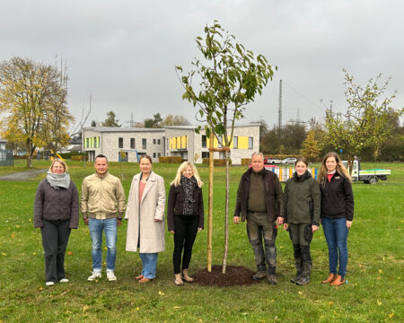 Sieben Personen stehen neben einem neu eingepflanzten Obstbaum