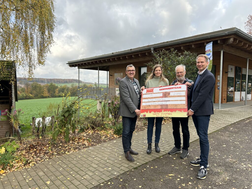 Vier Personen stehen vor einem Haus und halten einen Spendencheck in den Händen