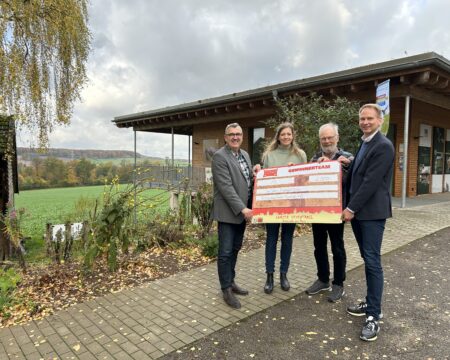 Vier Personen stehen vor einem Haus und halten einen Spendencheck in den Händen