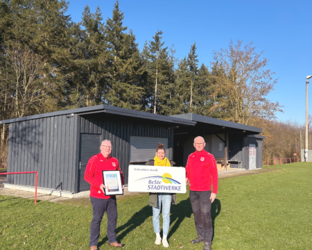 Eine Frau und zwei Männer stehen mit Urkunde und Schild vor Vereinsheim.