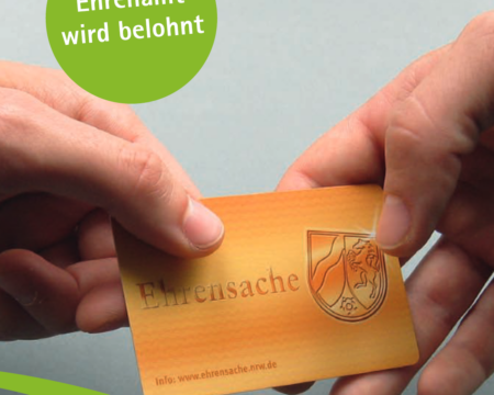 Zwei Hände halten eine goldene Karte in der Hand auf der Ehrenamtskarte steht.