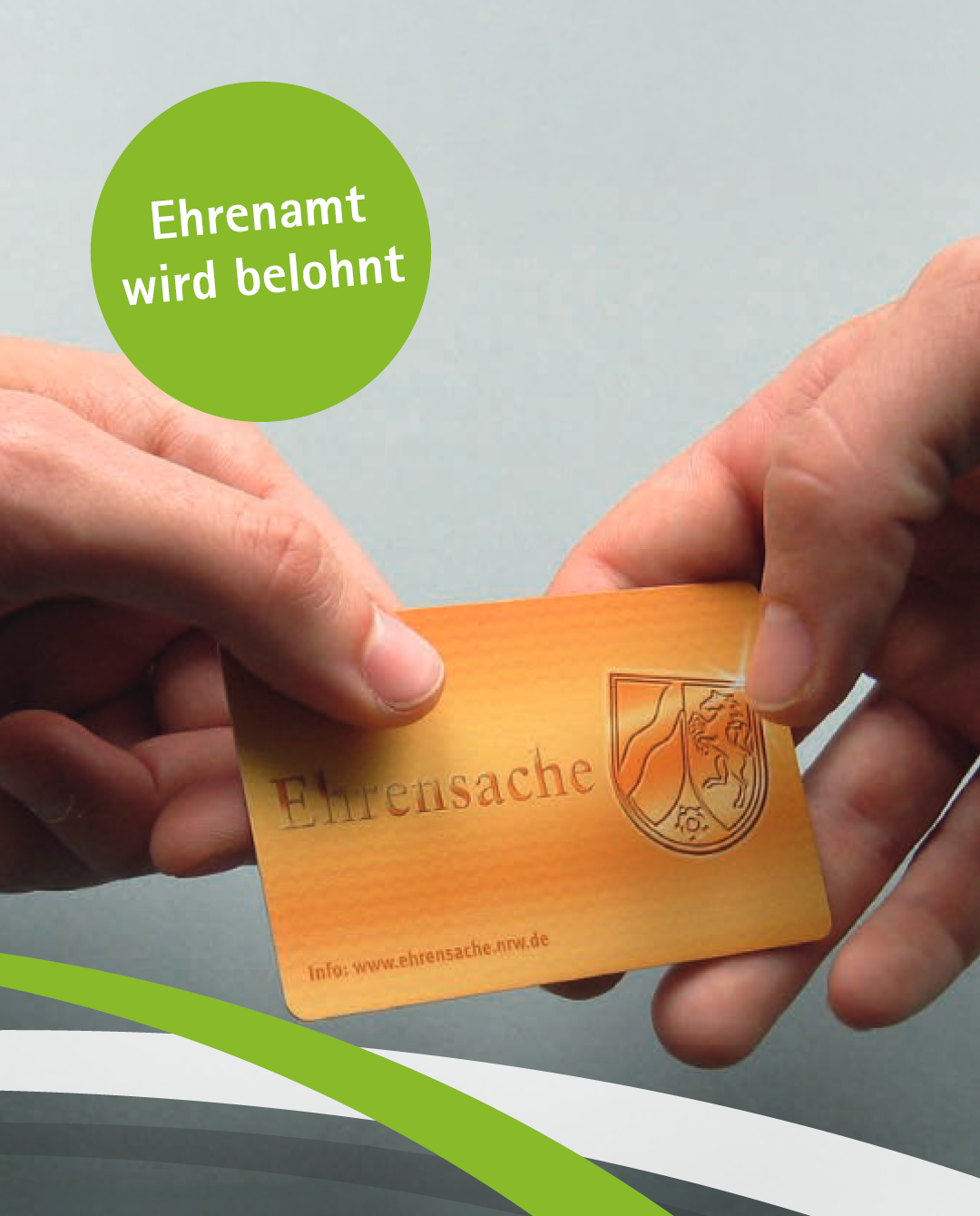 Zwei Hände halten eine goldene Karte in der Hand auf der Ehrenamtskarte steht.