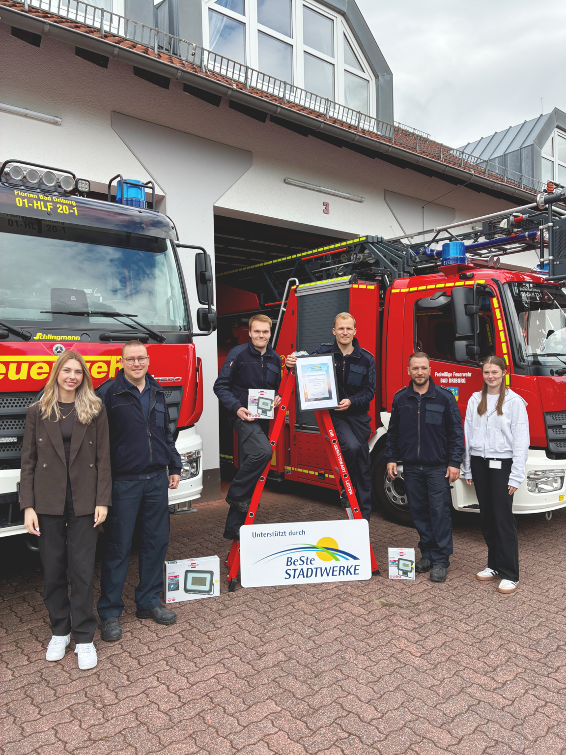 Sechs Personen stehen vor Feuerwehrfahrzeugen und präsentieren die Urkunde.