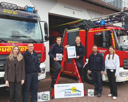 Sechs Personen stehen vor Feuerwehrfahrzeugen und präsentieren die Urkunde.