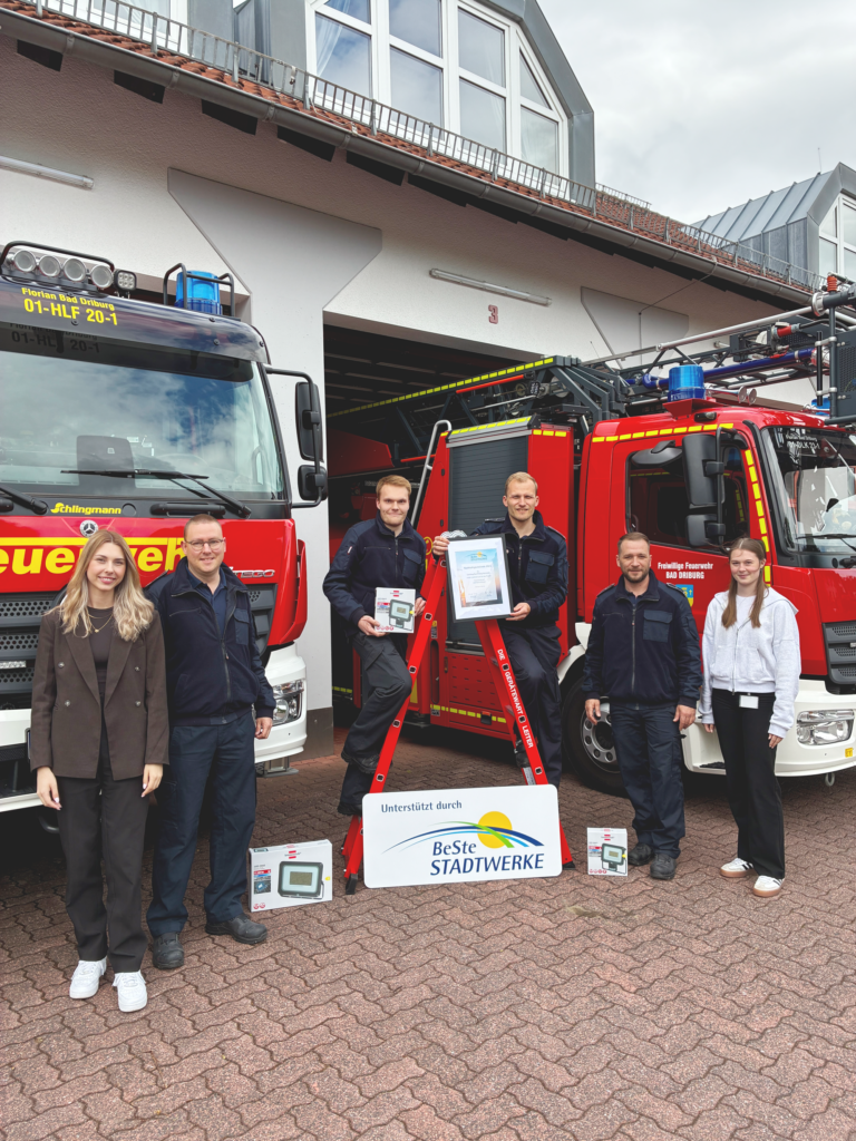 Sechs Personen stehen vor Feuerwehrfahrzeugen und präsentieren die Urkunde.