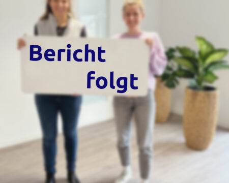 Zwei Frauen (unscharf) halten ein Schild in der Hand auf dem steht Bericht folgt