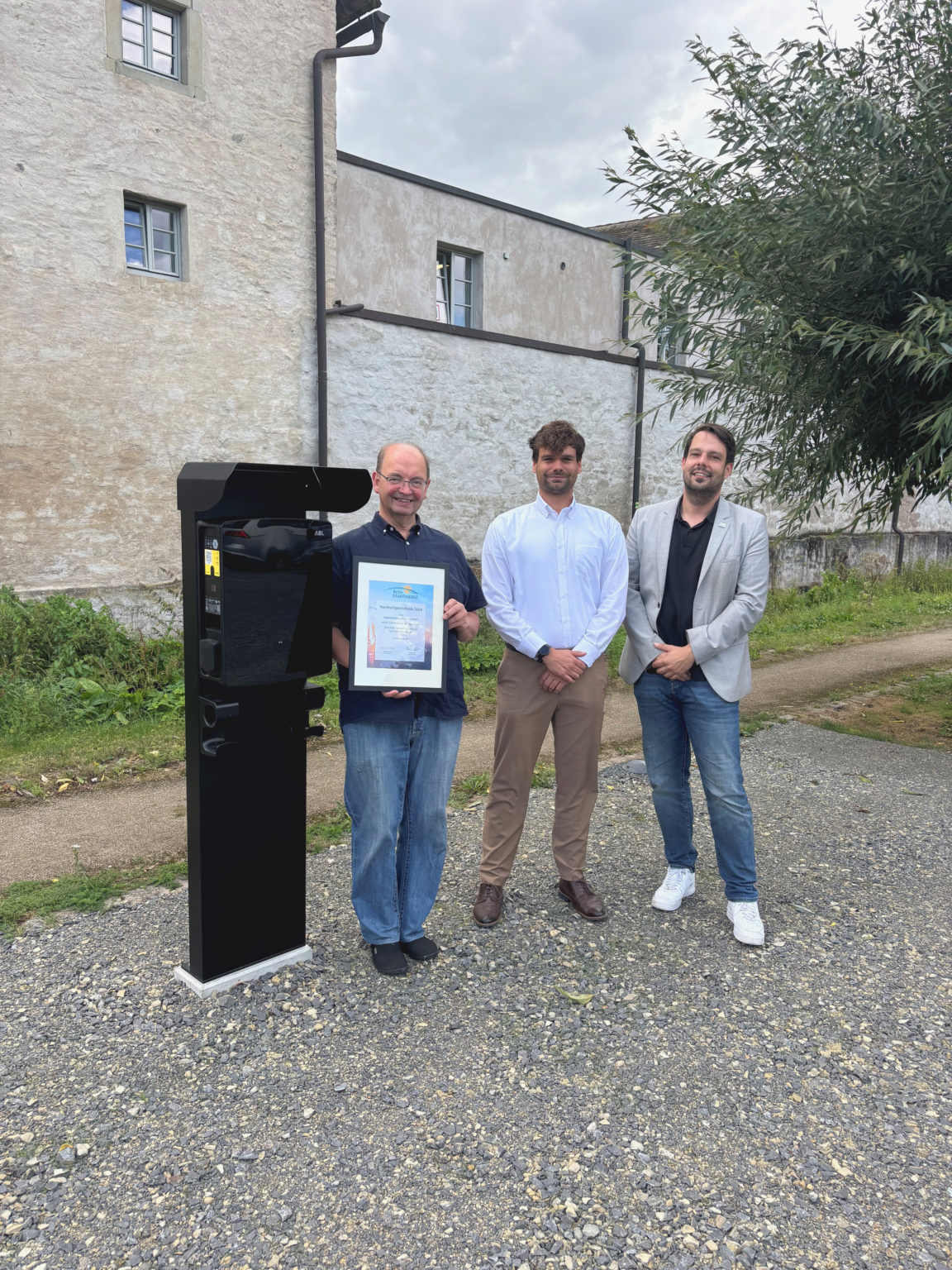 Drei Personen stehen neben einer Ladesäule für Elektrofahrzeuge