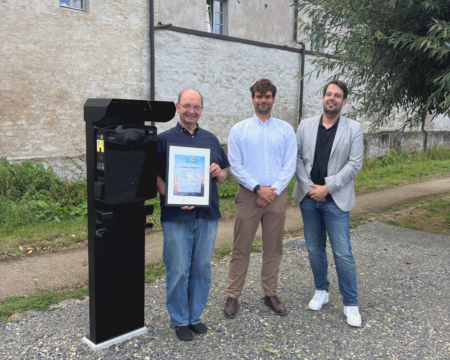 Drei Personen stehen neben einer Ladesäule für Elektrofahrzeuge