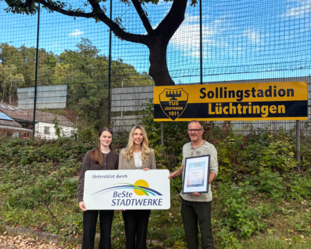 Zwei Frauen und ein Mann stehen vor einem Sportplatz